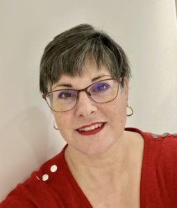 smiling pale skinned woman with short brown hair wearing glasses, red lipstick and a red sweater